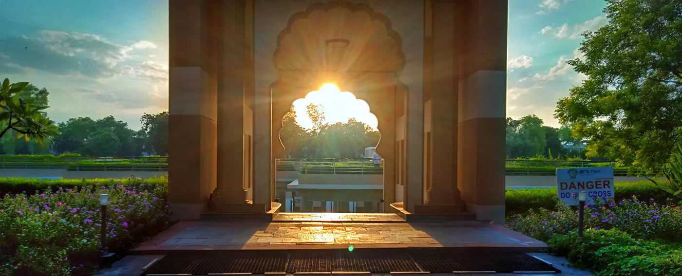 Low sunlight shines through a stone arch toward a garden.